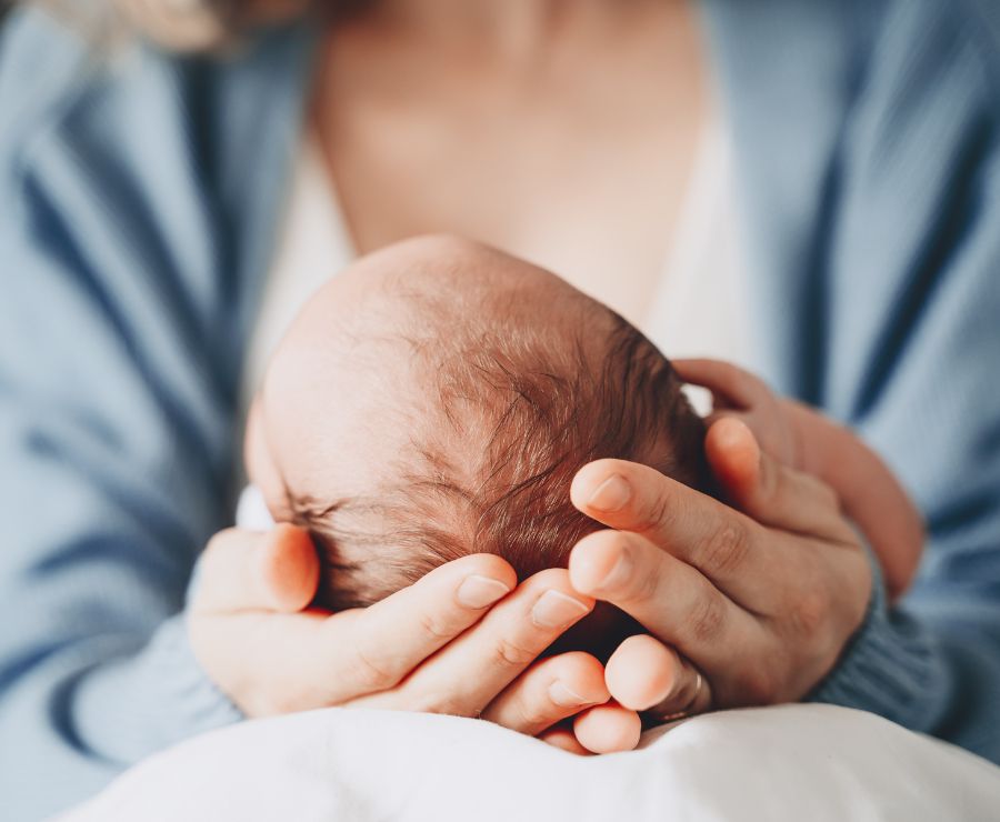 Ein Baby liegt mit seinem Köpfchen in den Händen seiner Mutter.