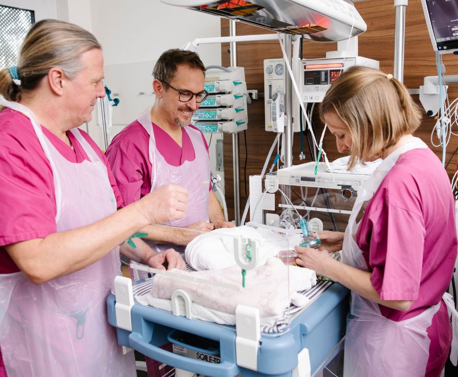 Ein Neugeborenes in einem Intensivbett wird von einem Ärzte-Team untersucht. 
