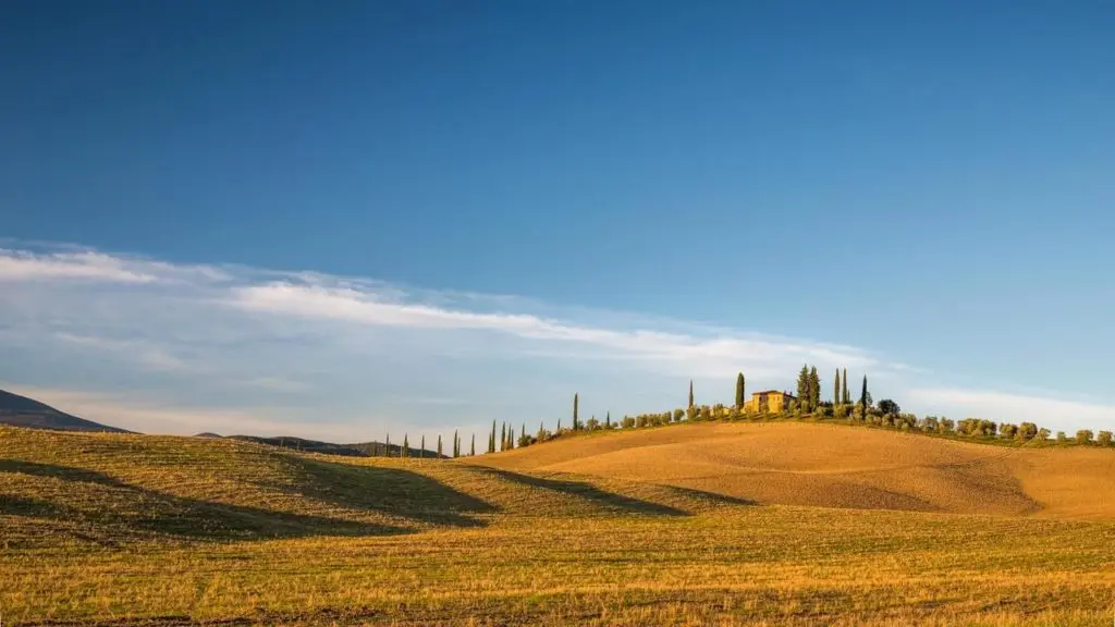 Hügelige Landschaft mit einem Haus und Bäumen im Hintergrund.