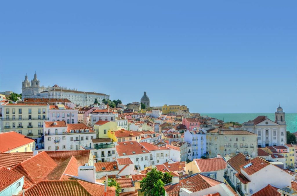 Häuser der Stadt Lissabon bei Sonnenschein und im Hintergrund das Meer.