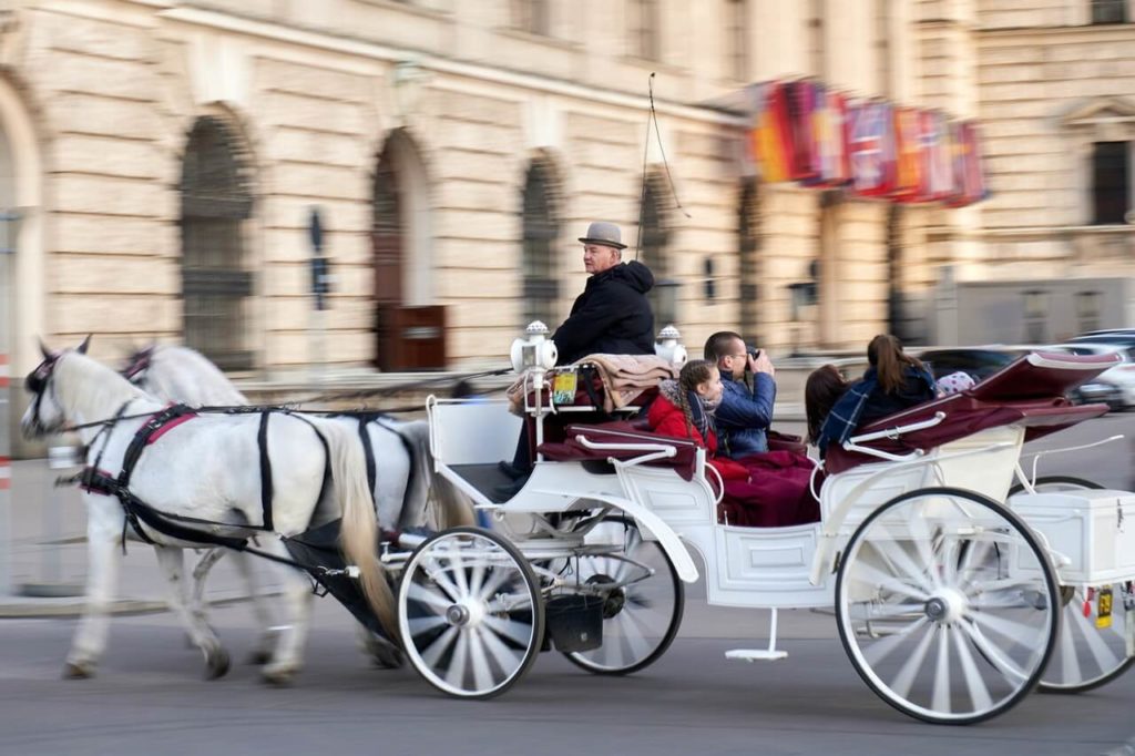 Eine weiße Kutsche mit weißen Pferden fährt durch die Straßen Wiens.