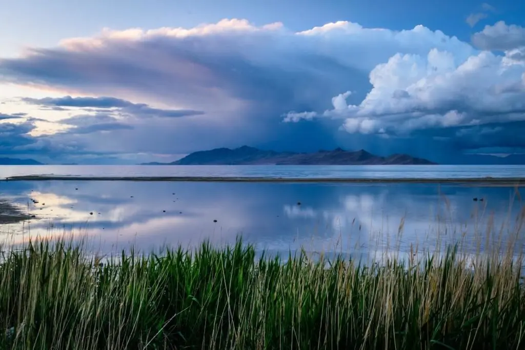Wolken spiegeln sich in einem großen See und im Hintergrund sieht man Berge.