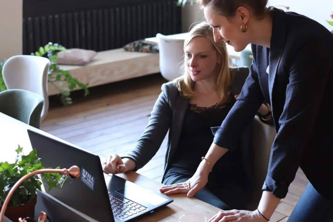 Kolleginnen vergleichen Reisekostenabrechnung Software am Laptop