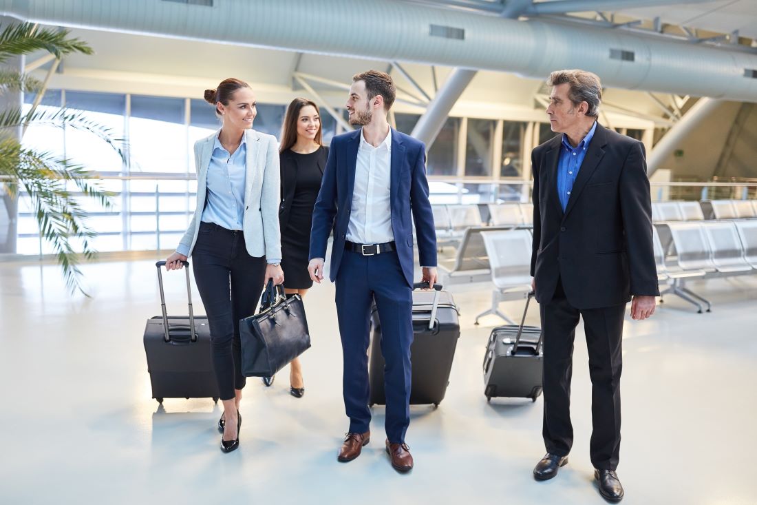 Vier Menschen mit Koffern laufen durch Flughafen und reden über die Defintion einer Dienstreise.