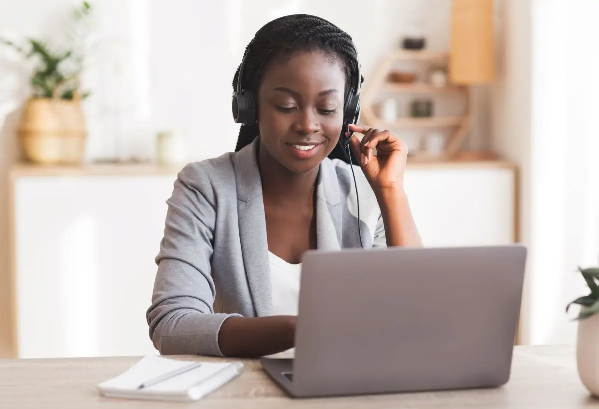 Frau mit Headset sitz an einem Laptop und arbeitet.