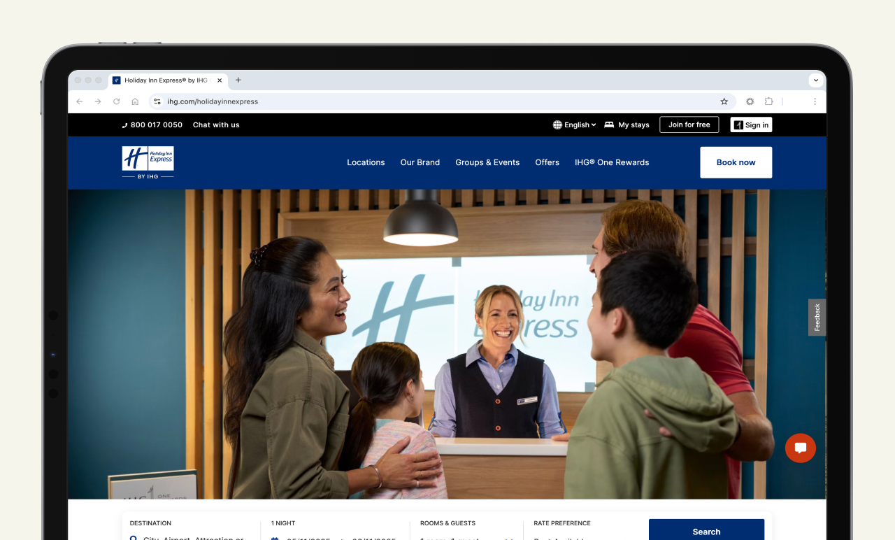 A family at a hotel check-in desk, smiling at the receptionist. The reception area has a "Holiday Inn Express" sign in the background.