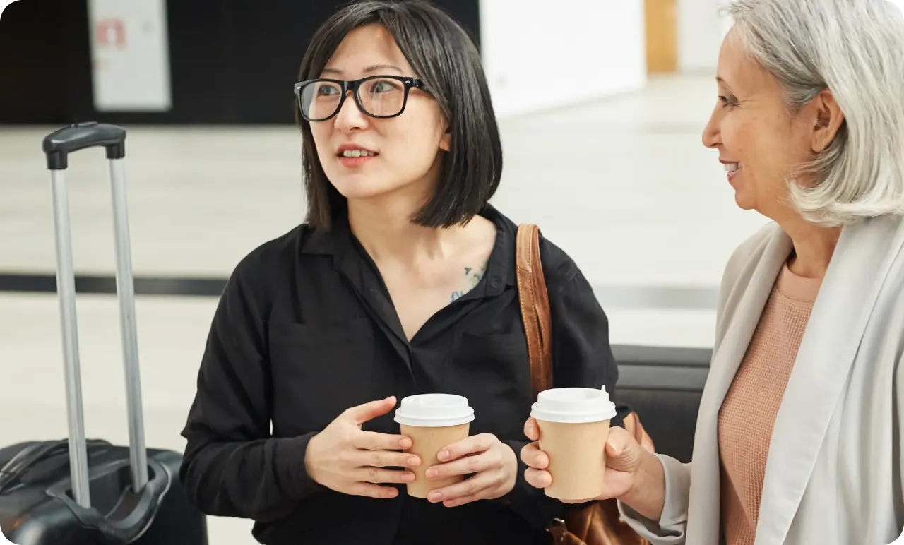 Two travellers waiting at an airport terminal drinking coffee.