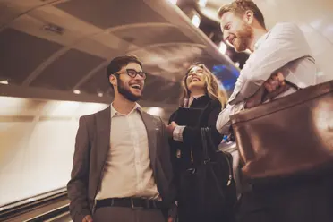 Drei junge Geschäftsleute stehen lachend an einem U-Bahnhof
