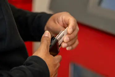 The hands of someone removing a payment card from a wallet, with a red and gray background.