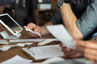 People at a desk reviewing receipts and documents, with a tablet on a stand nearby.