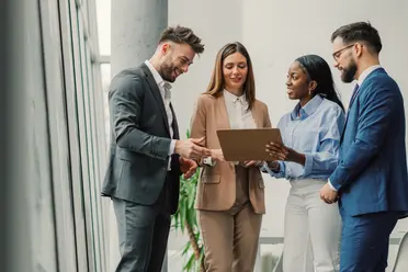Four professionals in formal attire discussing a document in a bright office setting.