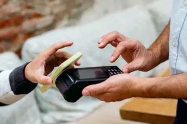 A person makes a contactless payment with a smartphone over a card reader held by another person.