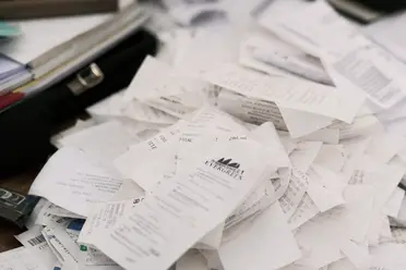 A messy pile of various printed receipts scattered on a table, alongside a closed black pen case and part of a folder.