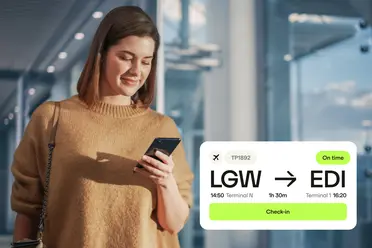 Woman at airport checking phone next to digital flight information showing LGW to EDI, flight TP1892, on time, check-in available.