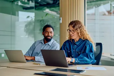two corporate workers looking at one laptop screen whilst typing