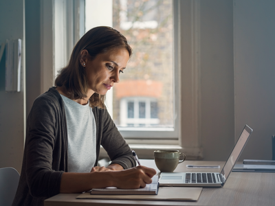 Adult at home, focused on a notebook in natural daylight.