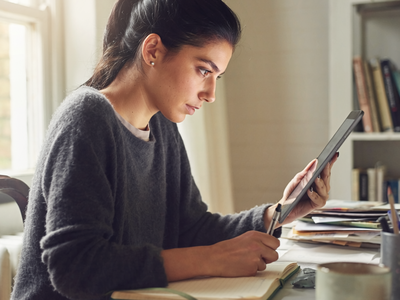 South Asian adult at home, focused on a notebook in natural daylight.