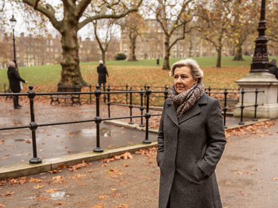 Woman in her fifties walking through an autumnal London park.