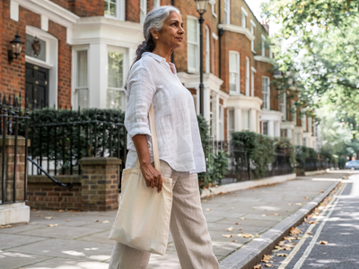 Woman in her early fifties walking through a leafy West London residential street on a bright morning.