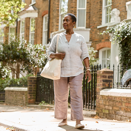 A woman walking past brick townhouses on a sunny London street