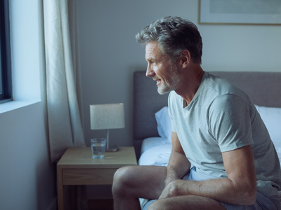 Adult sitting on the edge of a bed in a calm London bedroom in the morning.