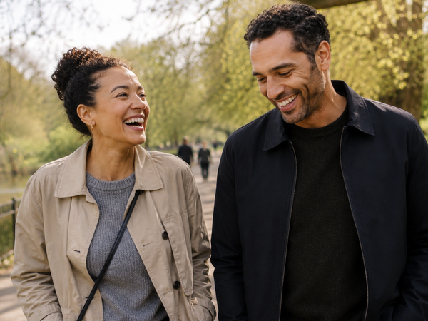 A mixed-heritage couple in their late thirties laughing on a walk through a London park.