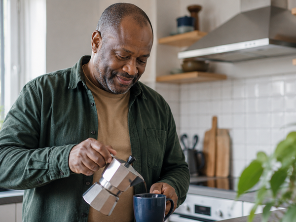 A Black British man in his early fifties making coffee in a bright kitchen.
