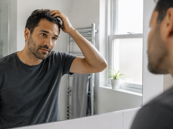 A man in his mid thirties finishing his grooming routine at home.