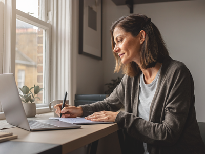 Adult at home, focused on a notebook in natural daylight.