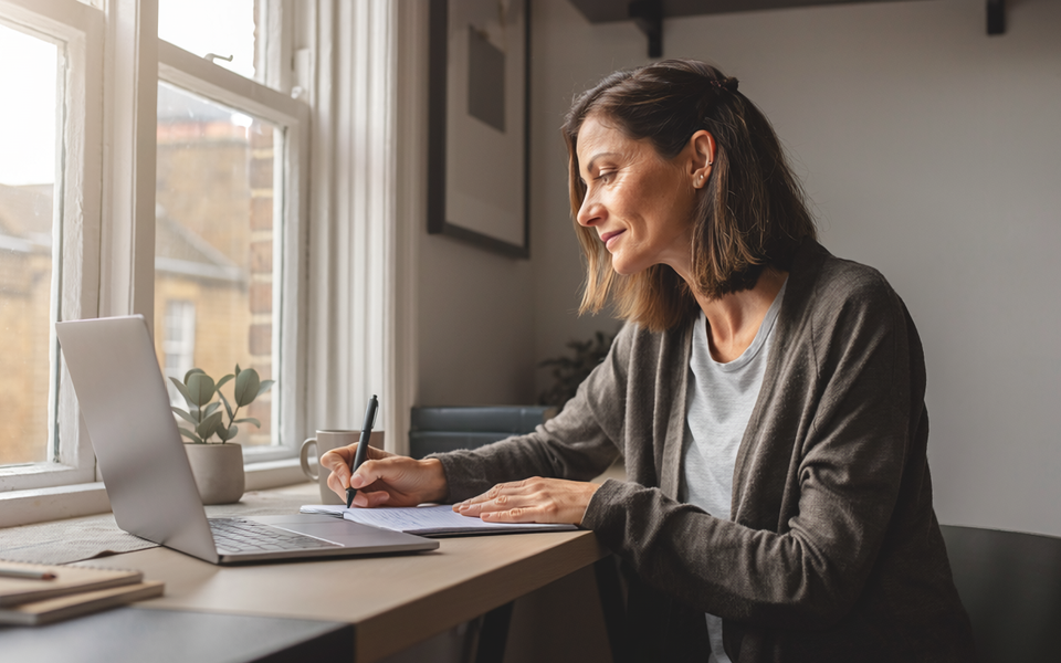 Adult at home, focused on a notebook in natural daylight.