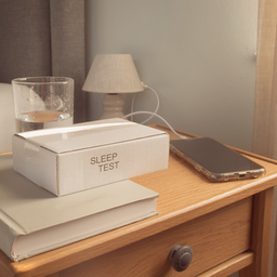 A home sleep test kit on a bedside table with a glass of water and a phone
