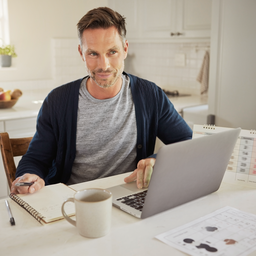 Adult at a kitchen table with a laptop and notebook, organising the day.
