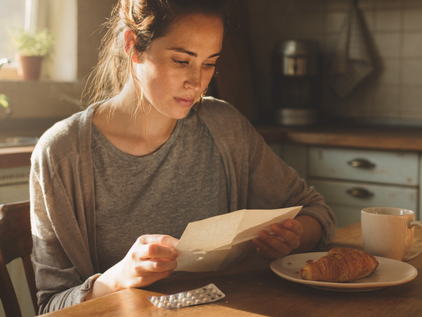Woman in her twenties reading a note at a kitchen table.