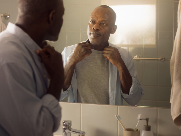 Man getting ready at a bathroom mirror in morning light.