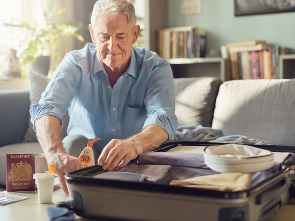 A man in his fifties packing a suitcase beside an open UK passport and travel essentials.