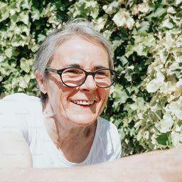 an older woman wearing glasses sitting on a bench