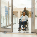 Wheelchair user and companion entering a bright, step-free healthcare area.
