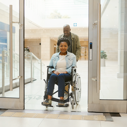 Wheelchair user and companion entering a bright, step-free healthcare area.