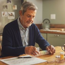 A middle-aged person organising medication and a health calendar at home, capable and calm
