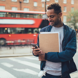 A newcomer to the UK in their late 20s with documents and a phone, finding their way in a bright city setting