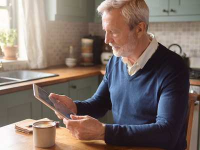A man in his sixties reading a wellness chart on a tablet at a sunlit kitchen table.