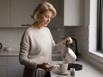 Woman in her fifties at home in a calm kitchen, making tea in the morning light.