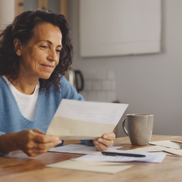 A person thoughtfully reviewing medical letters at a kitchen table, considering their options