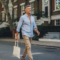 Man in his late forties walking along a leafy residential London street on a sunny weekday morning.