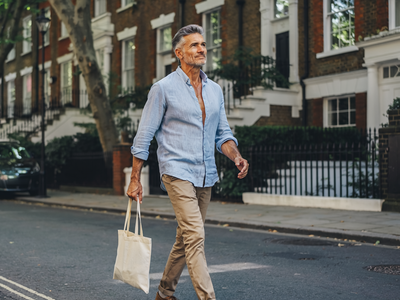 Man in his late forties walking along a leafy residential London street on a sunny weekday morning.