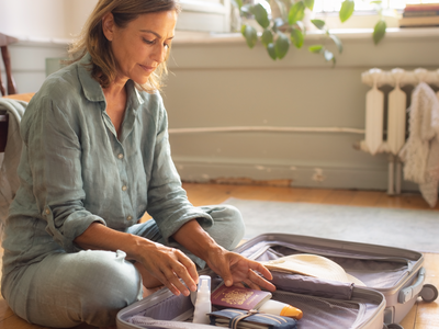 A mixed-heritage woman packing a suitcase beside an open UK passport and travel essentials.