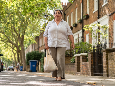 Woman in her fifties walking through a leafy West London street on a bright morning.