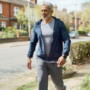 A South Asian man in his 50s walking outdoors for his heart health, fitness tracker on wrist, bright daylight