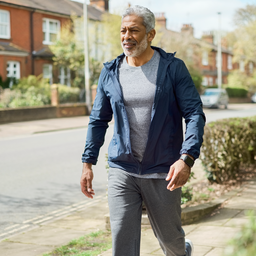 A South Asian man in his 50s walking outdoors for his heart health, fitness tracker on wrist, bright daylight