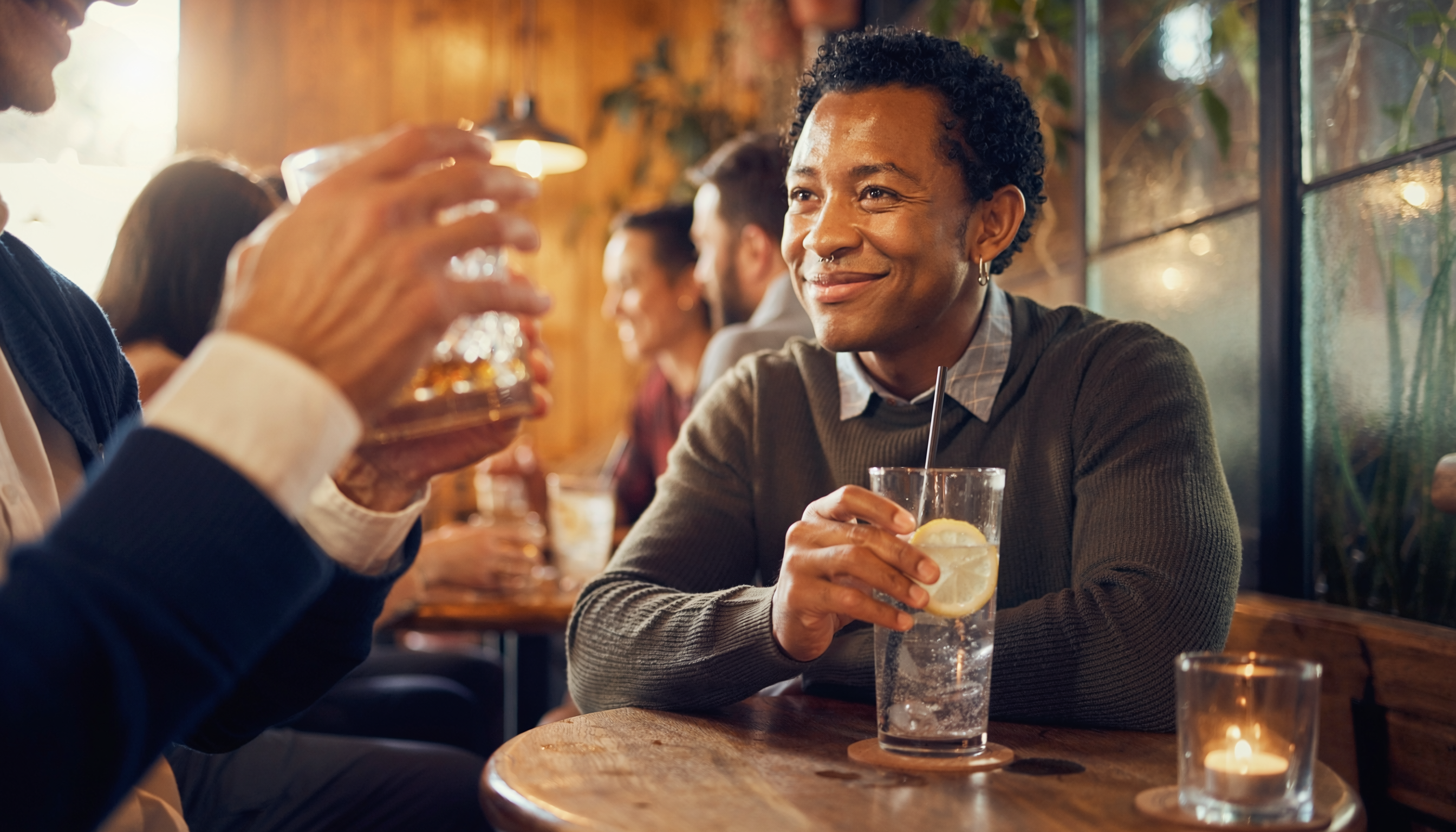 A young adult in their late 20s enjoying a social evening with a soft drink in hand, relaxed not isolated